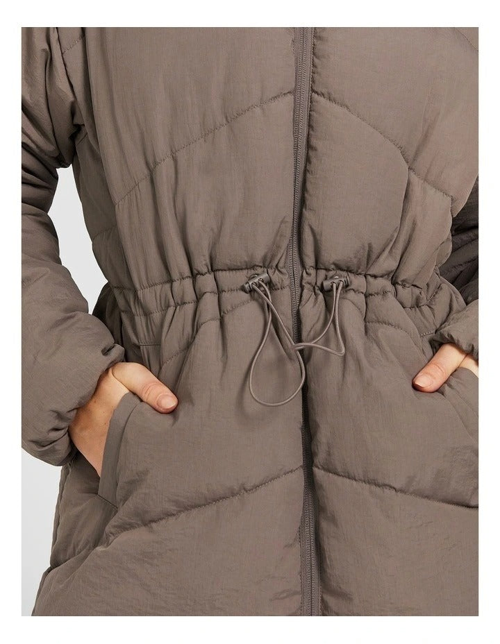 Rockwear Longline Puffer Jacket in Brown, women's full-length puffer jacket with side pockets, padded insulation, and elastic toggle waist for a flattering fit.
