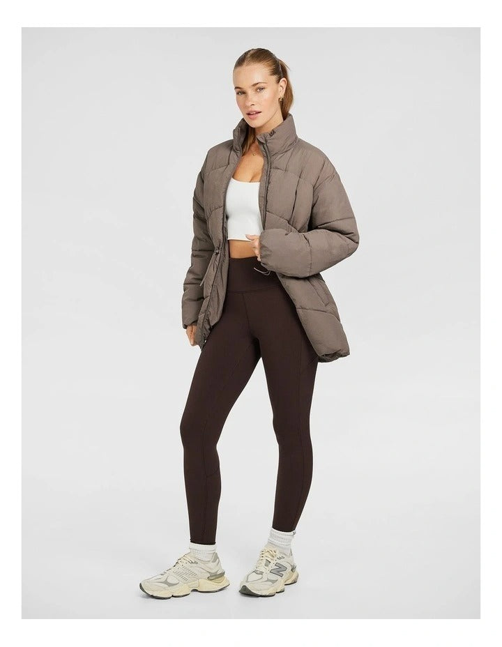 Rockwear Longline Puffer Jacket in Brown, women's full-length puffer jacket with side pockets, padded insulation, and elastic toggle waist for a flattering fit.