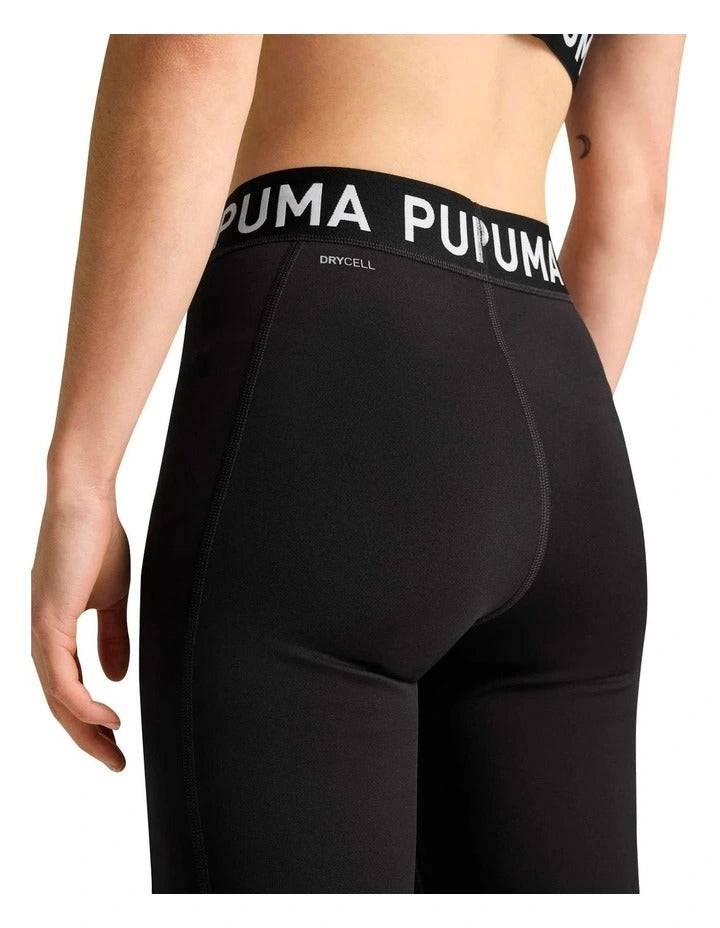 Person wearing black Puma leggings and sports bra holding a kettlebell on a white background