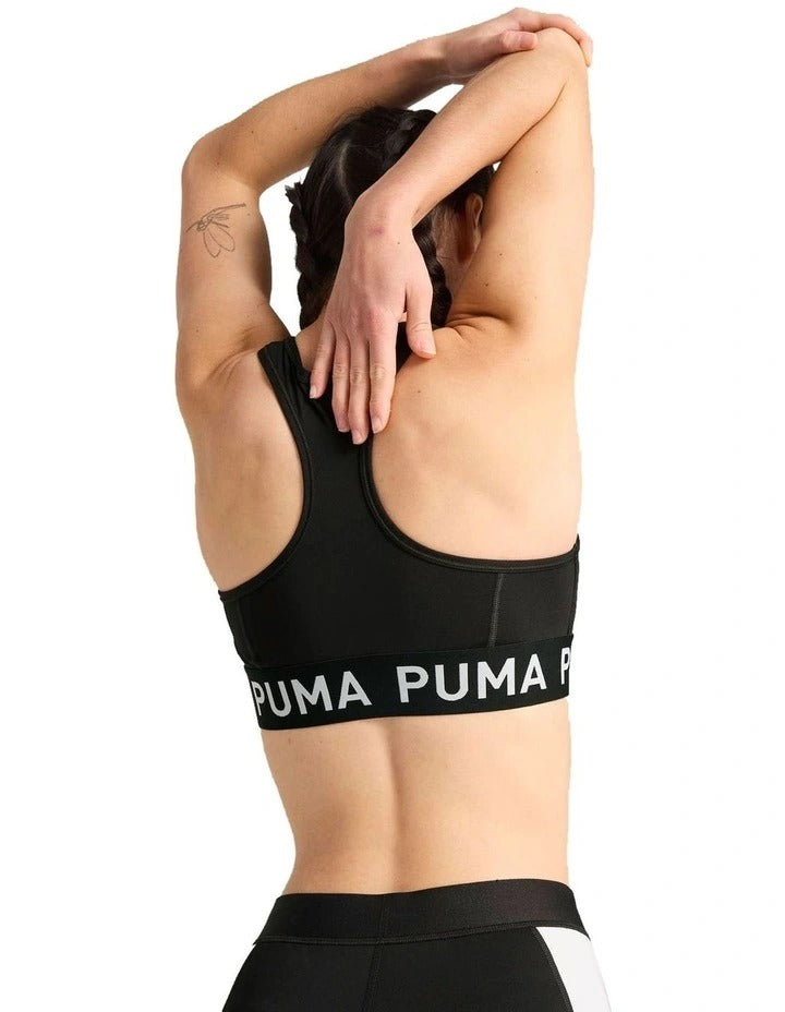 Woman wearing Puma sports bra and leggings holding a medicine ball on a white background