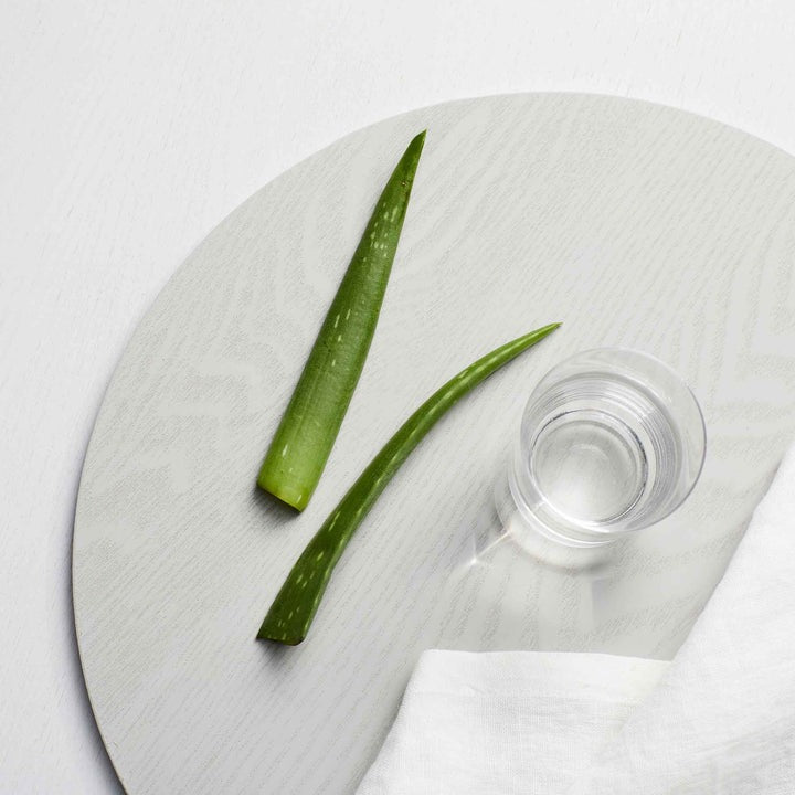 Aloe vera strip and a small bottle of clear liquid on a textured white surface