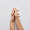 Two hands holding each other against a light gray background