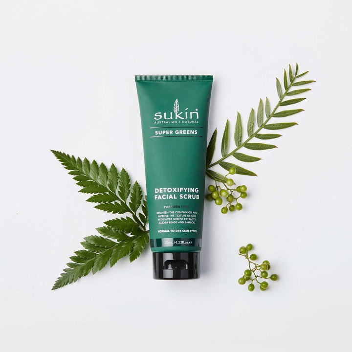 Sukin Super Greens Detoxifying Facial Scrub with green leaves and berries on a white background
