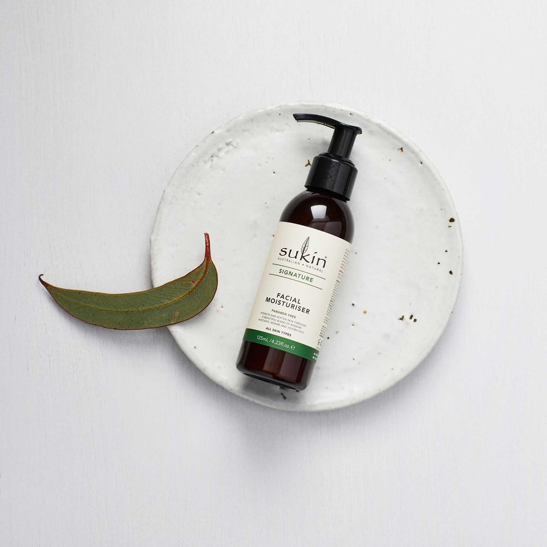 Sukin facial moisturizer bottle on a white background with a eucalyptus leaf.
