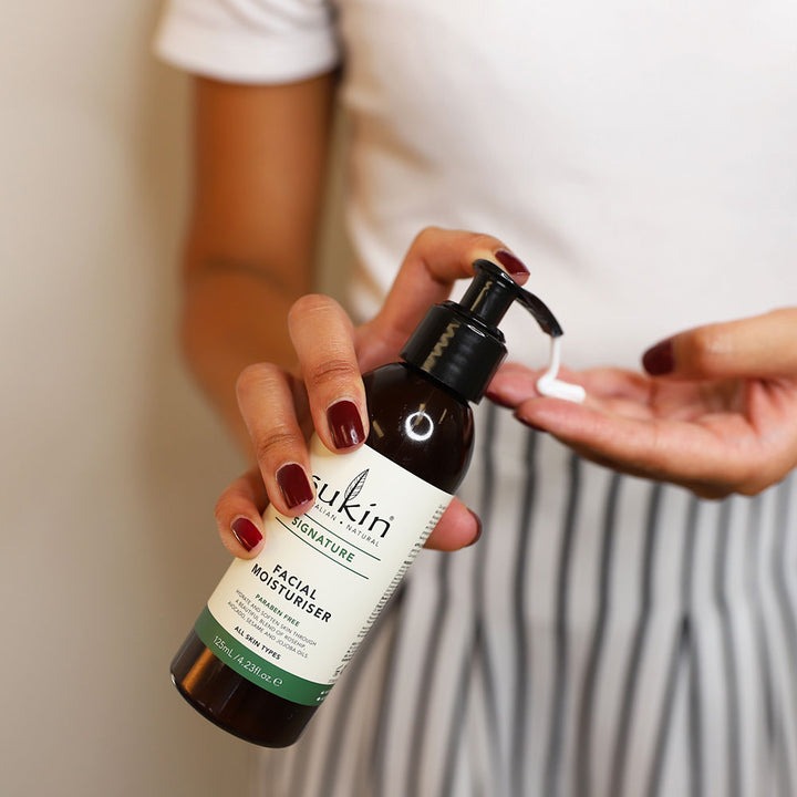 Person holding a bottle of Sukin facial moisturizer with a blurred background