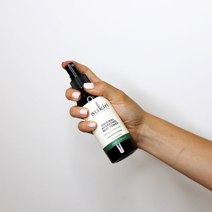 Hand holding a Sukin skincare product against a white background