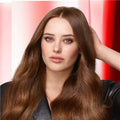 Woman with long, wavy brown hair against a pink and red striped background