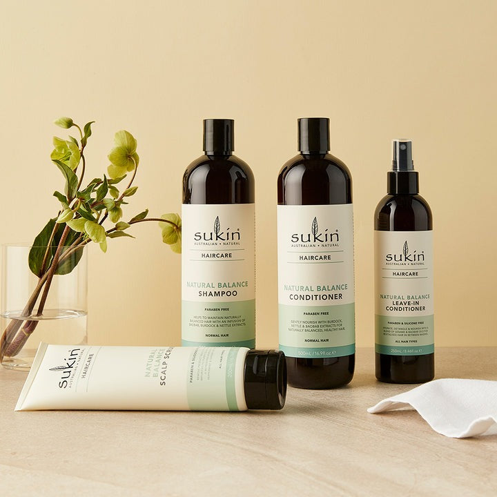 Sukin hair care products including shampoo, conditioner, and scrub on a wooden surface with a beige background.
