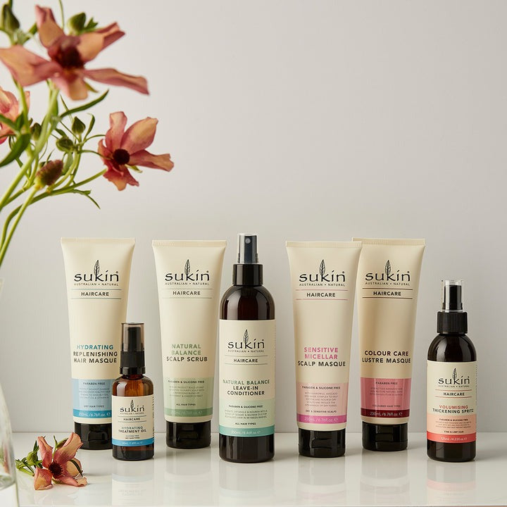 Sukin hair care products on a white surface with flowers in the background