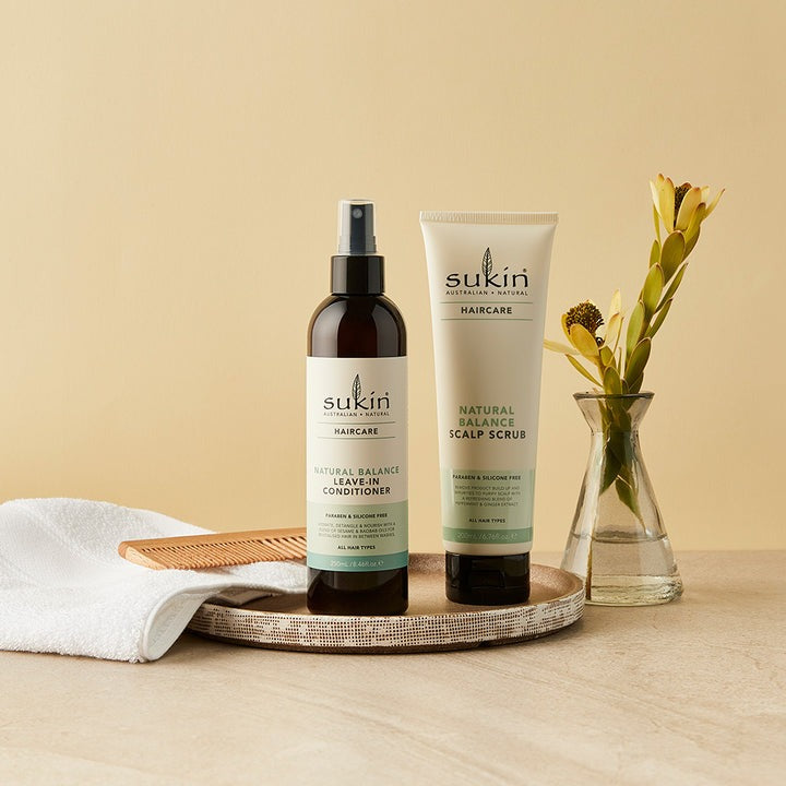 Sukin hair care products on a wooden tray with a vase of flowers on a beige background