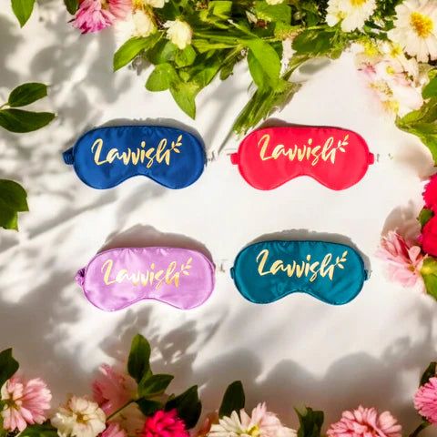 Lavvish sleep eye masks in blue, pink, teal, and purple colors surrounded by fresh flowers on a white background