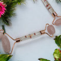 Lavvish Rose Quartz Facial Roller with box displayed on iridescent stand surrounded by small potted succulents