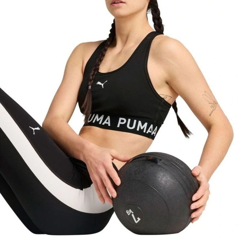 Woman wearing Puma sports bra and leggings holding a medicine ball on a white background