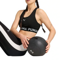 Woman wearing Puma sports bra and leggings holding a medicine ball on a white background