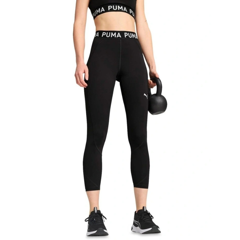 Person wearing black Puma leggings and sports bra holding a kettlebell on a white background