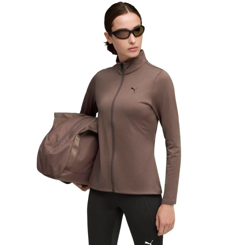 Woman wearing a brown athletic jacket and black leggings with a duffel bag on a white background