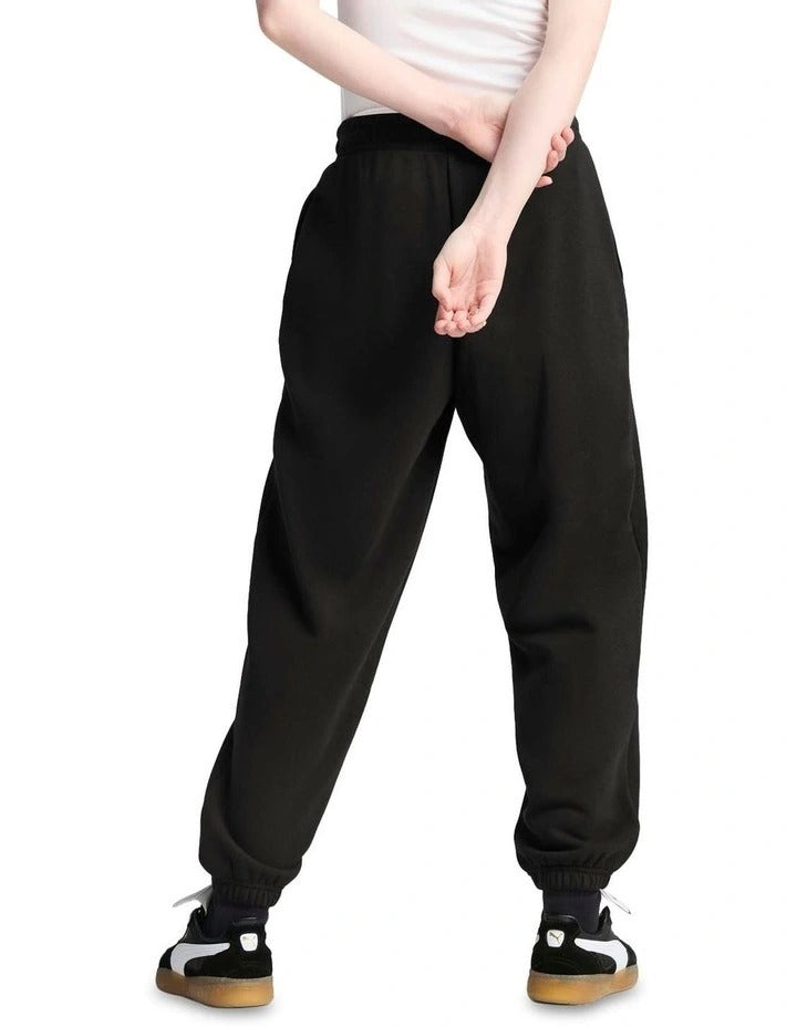 Person wearing black Puma pants and a white tank top, holding a black Puma handbag on a white background.