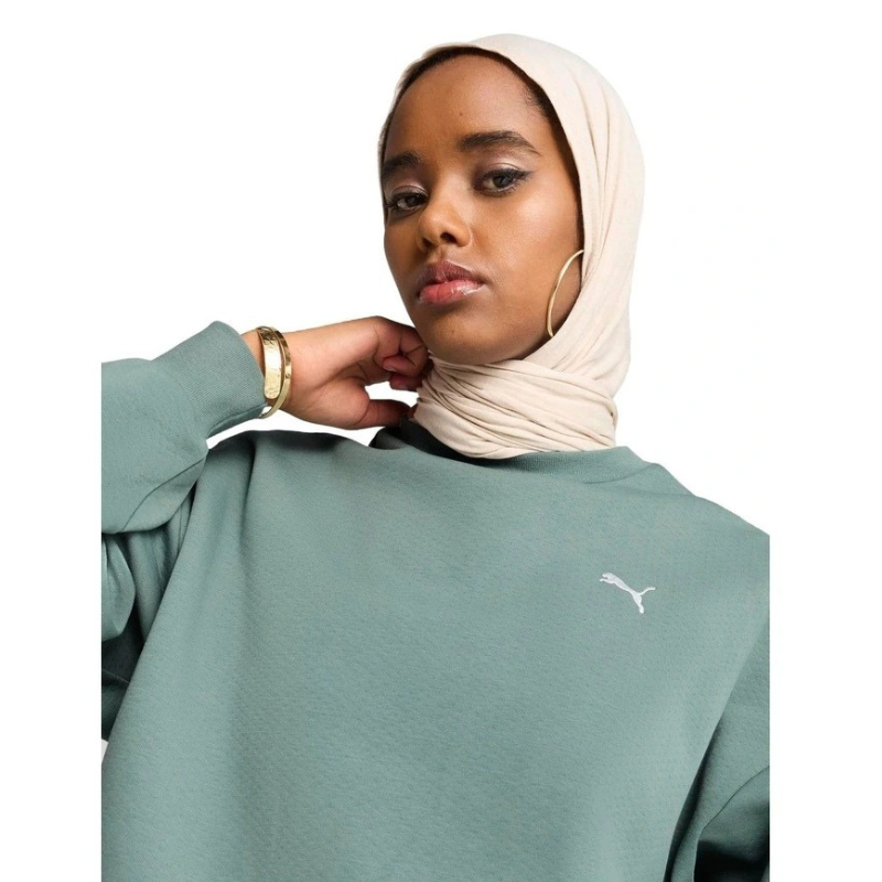 Woman wearing a green Puma sweatshirt with a beige hijab on a white background