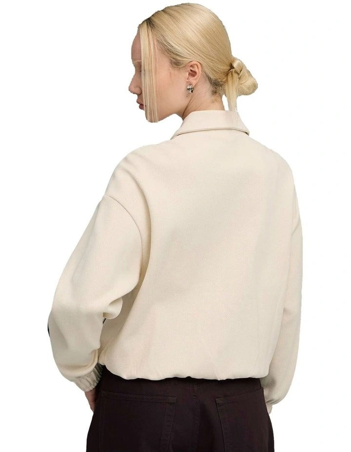 Person wearing a cream and green jacket with a brand logo on a white background