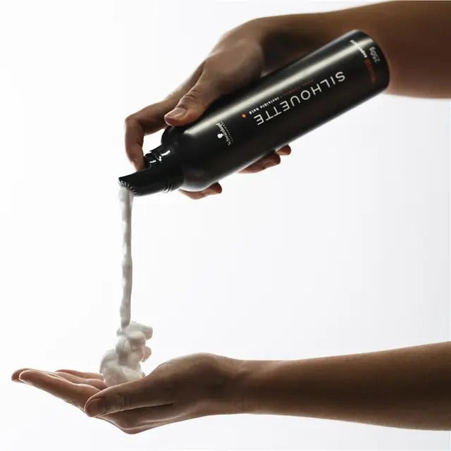 Person holding a 'Silhouette' hair product bottle pouring white foam into another hand against a white background