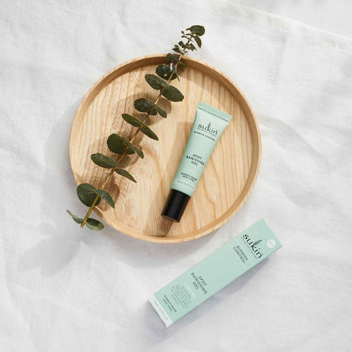 Sukin skincare product on a wooden plate with eucalyptus leaves on a white background