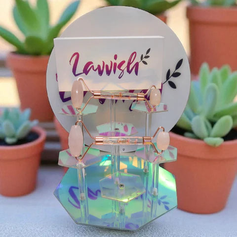Lavvish Rose Quartz Facial Roller with box displayed on iridescent stand surrounded by small potted succulents