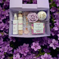 Purple Lavvish self-care gift box with skincare products, bath salts, soap bar, facial roller, and bath bomb displayed on purple floral background
